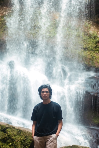 A man dressed in a black round collar shirt day stood near the waterfall
